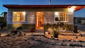 Una casa de dos pisos con puerta roja, ventanas amplias y un pequeño porche.