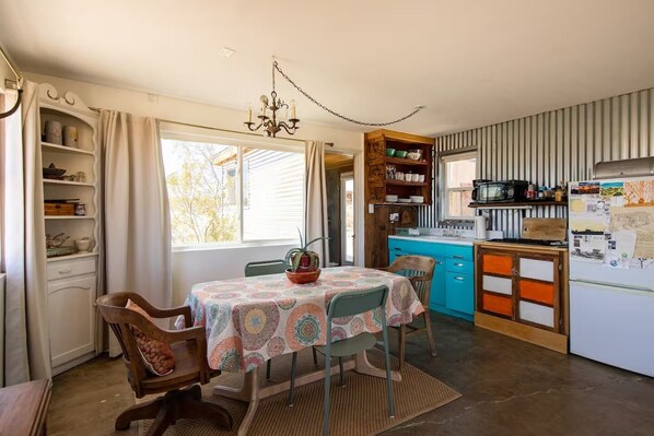A compact kitchen with a dining area, featuring a table with chairs, a chandelier, and a refrigerator with papers attached.