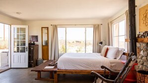 Un dormitorio con cama, banca de madera, escritorio, espejo y vistas al exterior.