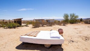 Una cama individual en un paisaje desértico, con un pequeño edificio al fondo.