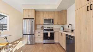 A modern kitchen with wooden cabinets, stainless steel appliances, and a granite countertop. - Chic 1 BR Urban Bungalow | AC + Free Parking (San Diego)