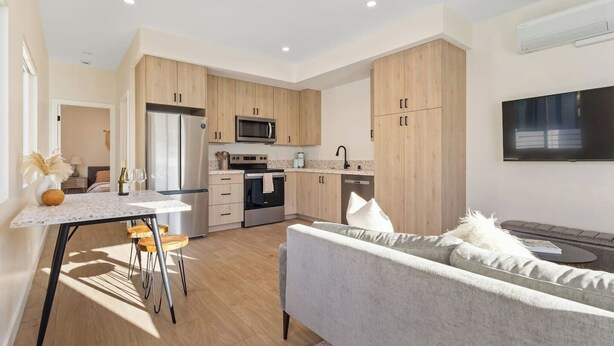A modern kitchen with wooden cabinets, stainless steel appliances, and a dining area with a table and chairs. - Chic 1 BR Urban Bungalow | AC + Free Parking (San Diego)