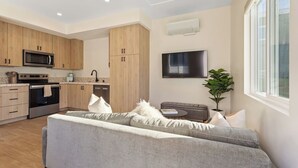 A modern kitchen with wooden cabinets, a microwave, oven, and a flat-screen TV. - Chic 1 BR Urban Bungalow | AC + Free Parking (San Diego)