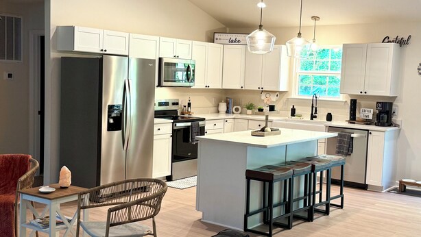 A modern kitchen with white cabinets, stainless steel appliances, and a central island with bar stools. - New & Cozy 5 BR Lake Anna Retreat - Large Game Room & Lake Access (Bumpass)