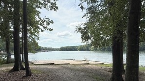 A lakeside campsite with a gravel area, wooden deck, and trees. - New & Cozy 5 BR Lake Anna Retreat - Large Game Room & Lake Access (Bumpass)