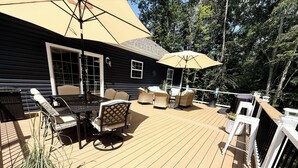 A wooden deck with outdoor furniture, including a table and chairs, and a large umbrella providing shade. - New & Cozy 5 BR Lake Anna Retreat - Large Game Room & Lake Access (Bumpass)
