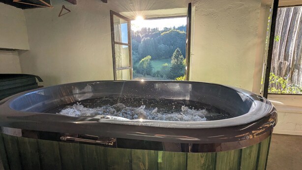 A hot tub with water bubbling, a wooden deck, and a view of a forest through a window. - The very isolated Vosges Mountain Chalet with private spa (Le Tholy)
