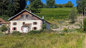 A rustic two-story house with a sloped roof, surrounded by a lush green landscape and a stone wall. - The very isolated Vosges Mountain Chalet with private spa (Le Tholy)