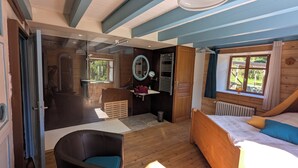 A wooden cabin room with a bed, a chair, a small sink, and a window with a view of greenery. - The very isolated Vosges Mountain Chalet with private spa (Le Tholy)
