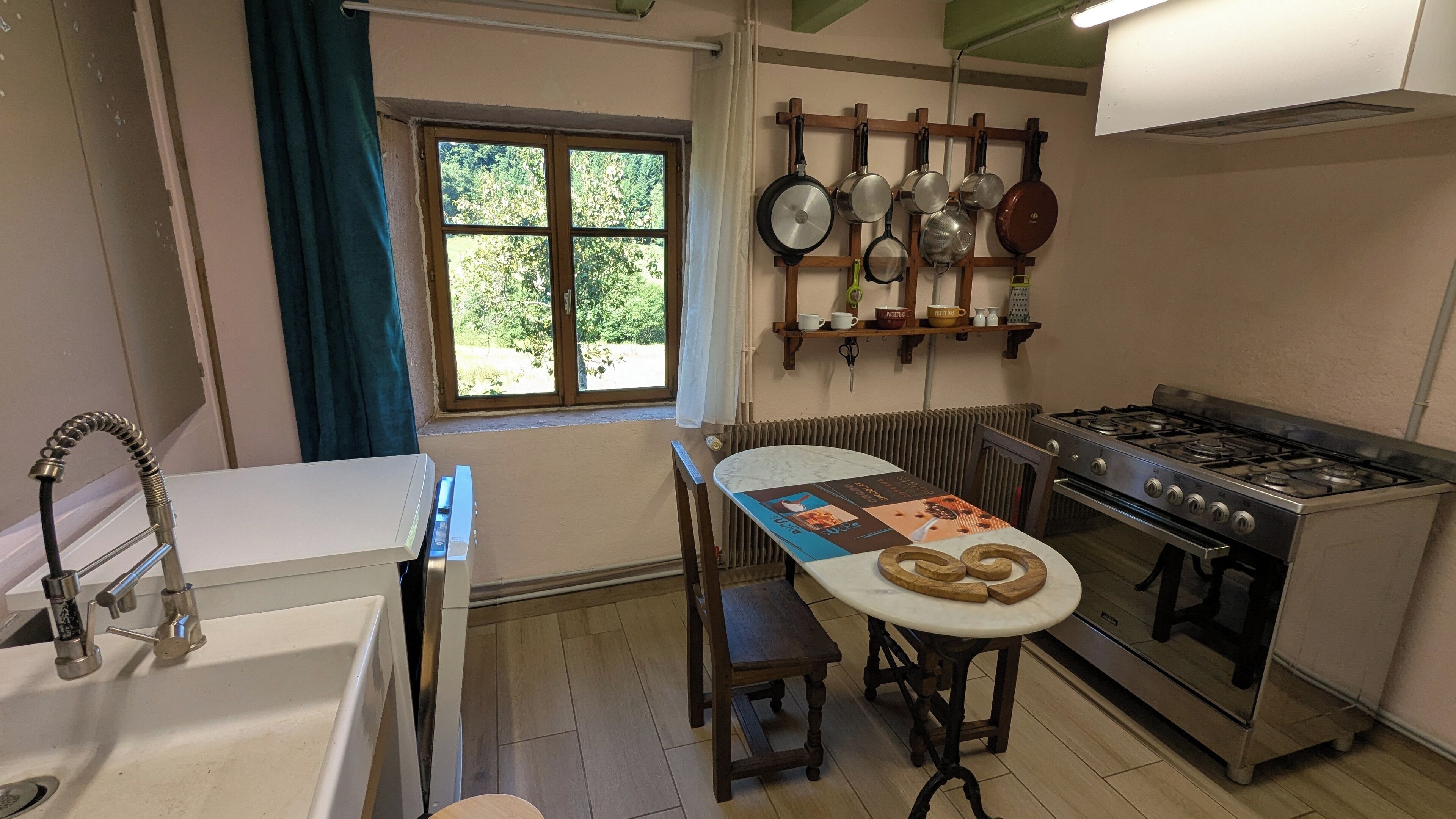 Une cuisine compacte équipée d’une cuisinière à gaz, d’un évier, d’une fenêtre avec des rideaux et d’un porte-ustensiles fixé au mur.