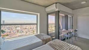 A modern hotel room with two beds, a balcony with a city view, a dining area, and an air conditioning unit. - Alma Rentals Huergo 475 (Buenos Aires)