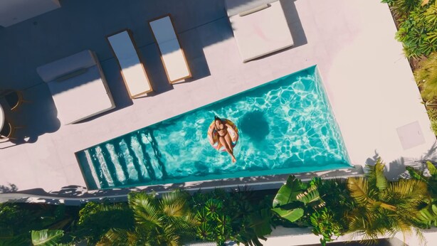En pool på taget med en person på en flydeplade, omgivet af liggestole og tropiske planter.