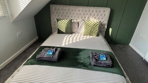 Une chambre à coucher avec un plafond haut, une tête de lit capitonnée, un lit avec une literie à rayures et deux oreillers.