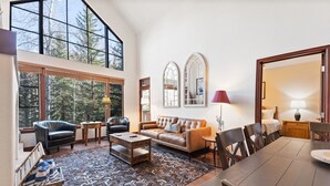 A spacious living room with a large window, a sofa, a coffee table, and a dining table with chairs. - Arrowhead at Beaver Creek, Direct Ski Access & A/C (Edwards)