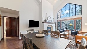 A spacious living room with a fireplace, a dining area with a large wooden table, and a cozy seating area with leather chairs. - Arrowhead at Beaver Creek, Direct Ski Access & A/C (Edwards)