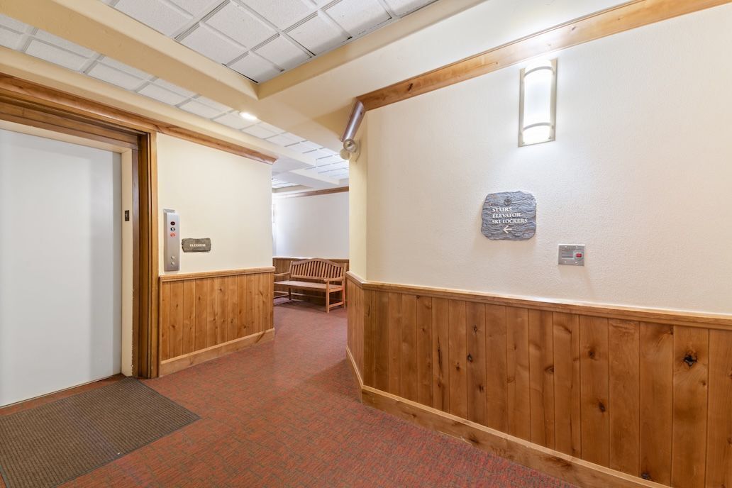 A hotel corridor with wooden paneling, a bench, and a sign indicating the elevator direction.