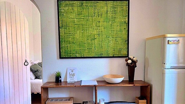 A modern kitchen with a wooden dining table, a large green abstract painting, a white refrigerator, and a small potted plant on the counter.