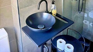 A bathroom with a round mirror, a black sink, and a glass-enclosed shower.