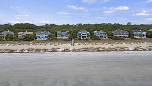 En fastighet vid stranden med flera hus, en sandstrand och en skogbeklädd kulle i bakgrunden.