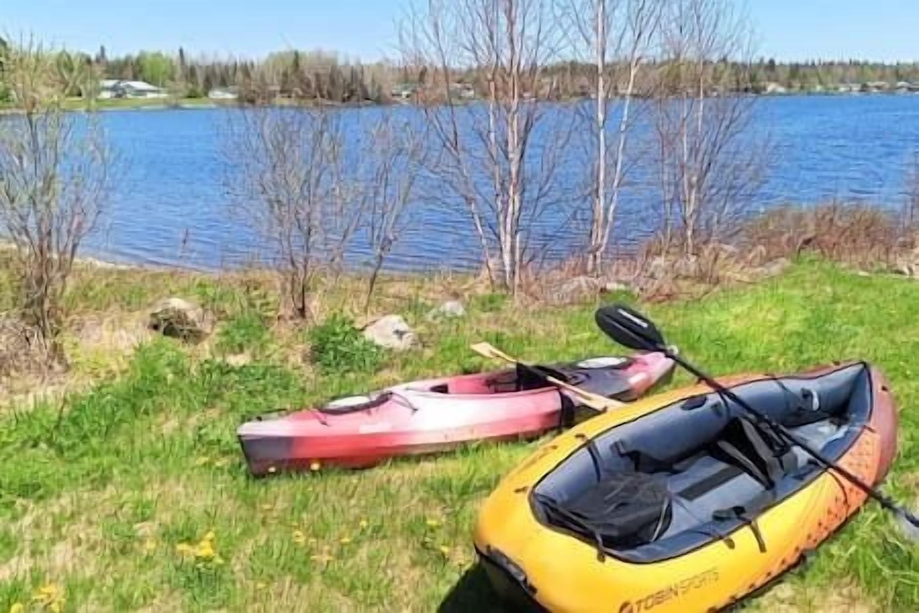 Un kayak et un canoë sont posés sur l’herbe, près d’une étendue d’eau.