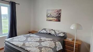 Ein Schlafzimmer mit einem Bett, einem Nachttisch, einer Lampe und einem Gemälde an der Wand.