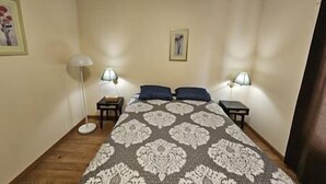 A bedroom with a patterned bedspread, two bedside lamps, a framed picture on the wall, and a small round table. - Restful stay at Obaska (Senneterre)