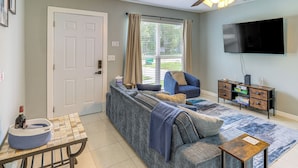 A living room with a sofa, a TV, a ceiling fan, and a window with curtains. - Fort Pierce Getaway: Near Marina Sq & Downtown! (Fort Pierce)