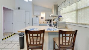 Cocina con armarios blancos, microondas y pileta. Hay dos sillas de madera y una mesa con un mantel individual.