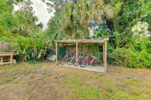 Ein überdachter Fahrradständer in einem Garten mit verschiedenen Pflanzen und einem Holztisch.