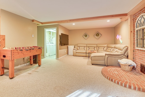 A cozy living room with a foosball table, a beige sofa, and a brick fireplace.