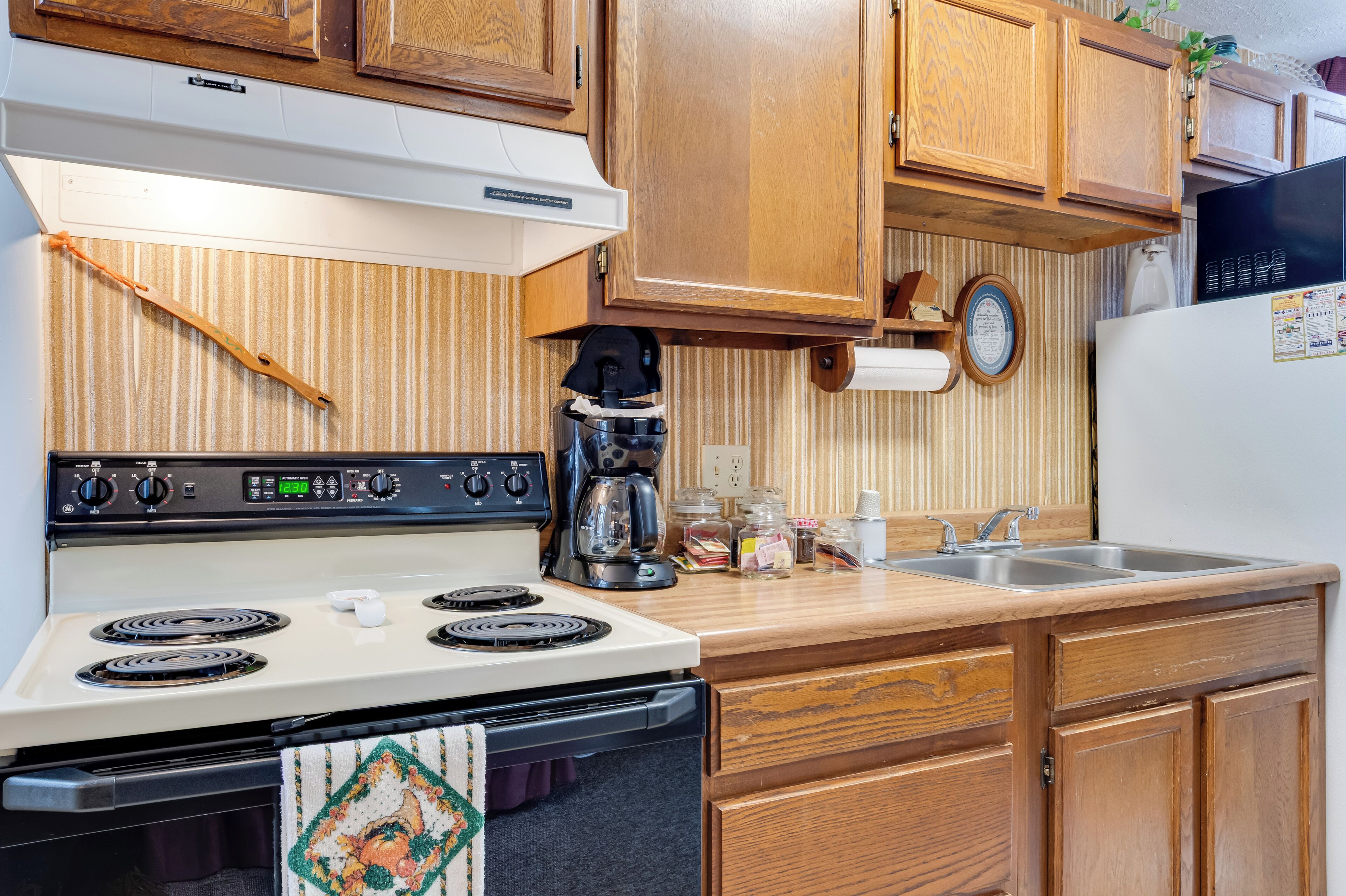Une cuisine avec des meubles de rangement en bois, une cuisinière blanche, une machine à café et un évier.