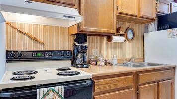 Une cuisine avec des meubles de rangement en bois, une cuisinière blanche, une machine à café et un évier.