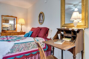 A bedroom with a bed, a desk, a chair, a lamp, a mirror, and a shelf with books.