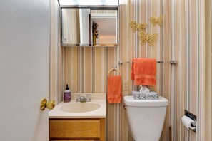 A bathroom with a striped wall, a sink, a toilet, and two orange towels.