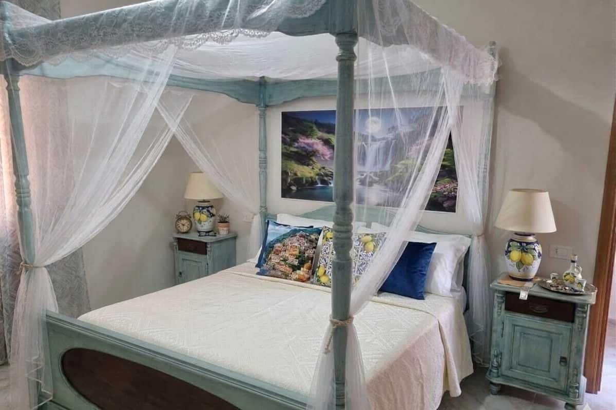 A four-poster canopy bed with a white bedspread and multiple pillows. There are two bedside tables with lamps and decorative items.