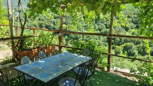 A table and chairs set under a pergola with a view of a lush green landscape. - Giordano Rooms Amalfi Coast  (Tramonti)