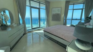 Ein geräumiges Schlafzimmer mit einem großen Bett, einem Schreibtisch und einem Stuhl. Mehrere Fenster bieten Blick aufs Meer.