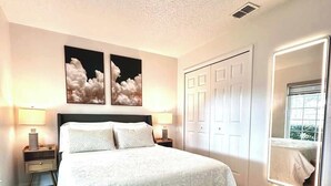 Ein Schlafzimmer mit einem großen Bett, Nachttischen, einer Bank, einem Spiegel und Kunstwerken an der Wand.