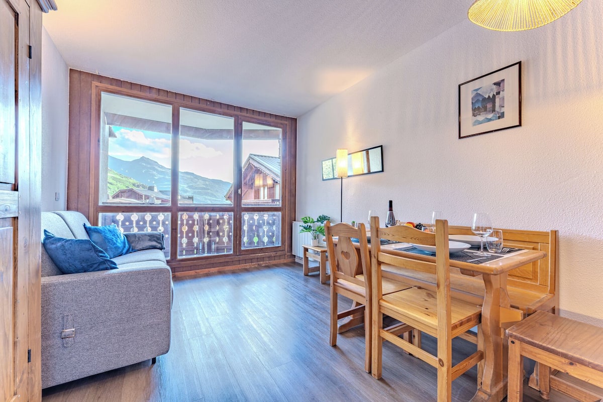Une pièce chaleureuse avec un canapé, une table à manger en bois, des chaises et une vue sur les montagnes grâce à de grandes fenêtres.