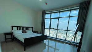 Un dormitorio con cama, mesita de noche, televisor sobre un mueble bajo y un ventanal con vista a la ciudad.