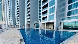 A modern building with a swimming pool, featuring a tiled deck and a glass facade.