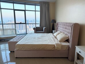 A bedroom with a large window, a bed, a chair, and a nightstand.