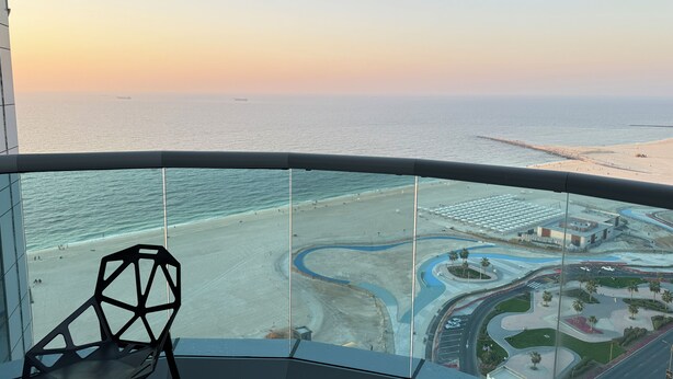 A high-rise hotel room with a balcony overlooking a beach and marina.