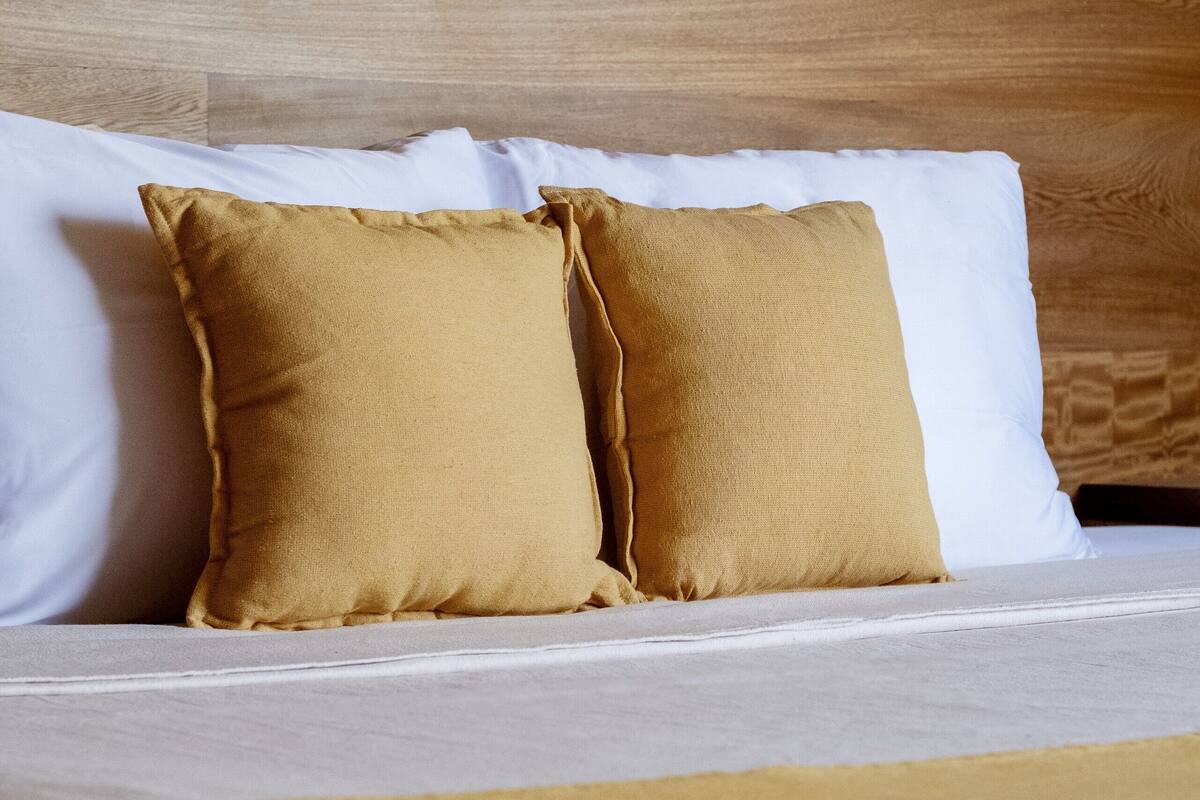 A bed with white and mustard-colored pillows, a wooden headboard, and a mustard-colored bedspread.