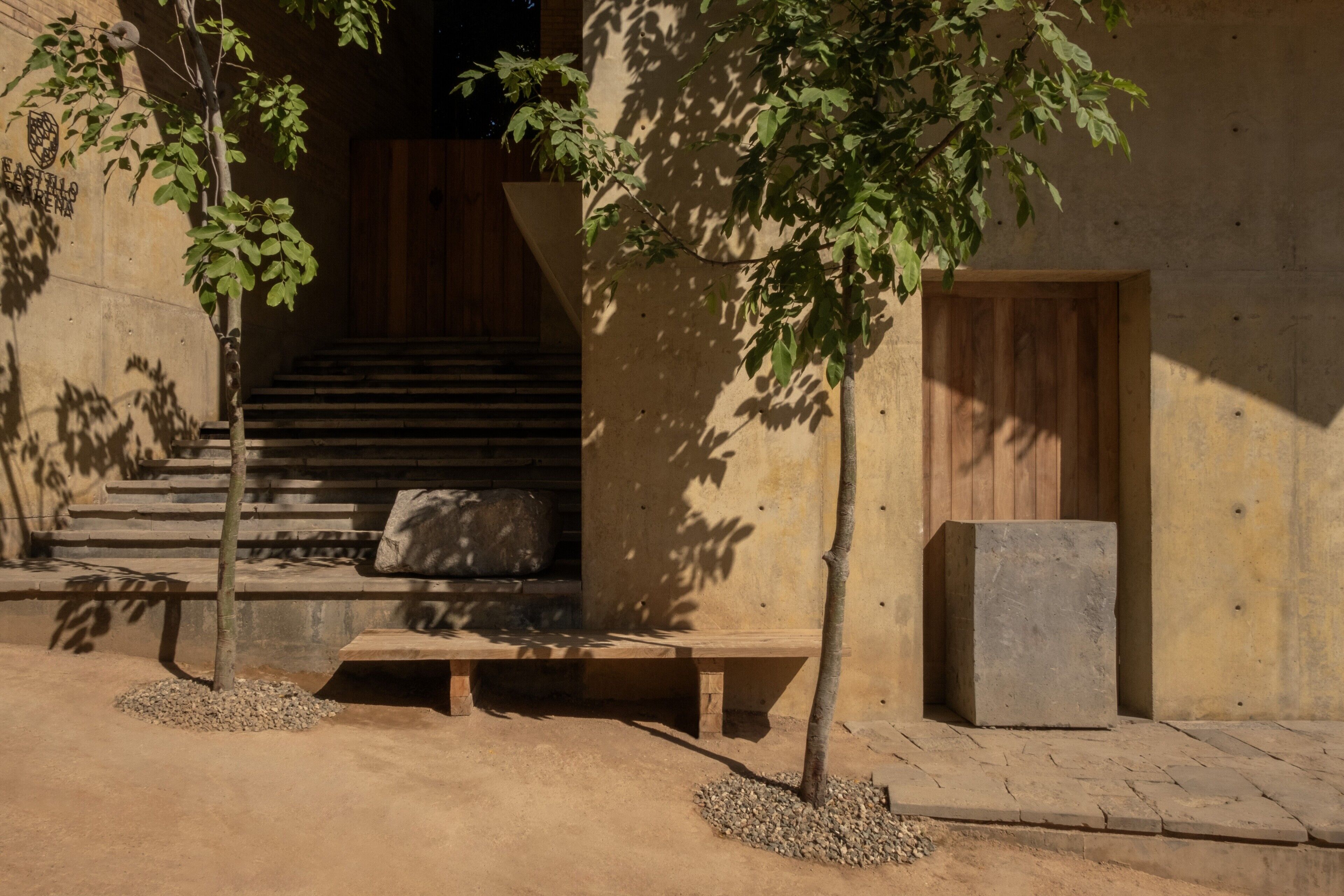 A building with a staircase leading to a wooden door, surrounded by trees and a bench.