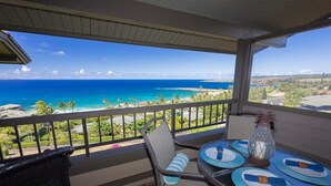 Un balcón con una mesa lista para dos personas, con vistas a una playa de aguas azules y tierra a lo lejos.