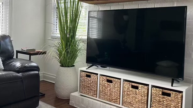 Uma sala de estar moderna com uma grande televisão de tela plana, um sofá de couro, uma planta em vaso e uma estante rústica de madeira acima da TV.