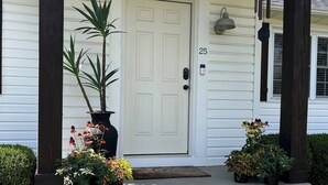 Uma casa branca com porta frontal, número 25, e varanda com plantas em vasos.