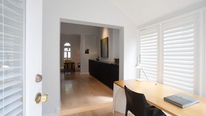 A modern interior with a wooden dining table, a black chair, and a book on the table. There is a kitchen area with a dark countertop and a painting above it. - Petite Maison, Potts Point Isyd (Potts Point)