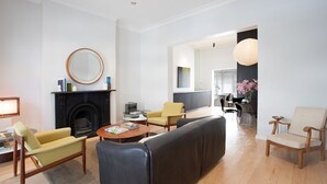 A modern living room with a fireplace, a dining area, and a kitchen visible through an open doorway. - Petite Maison, Potts Point Isyd (Potts Point)